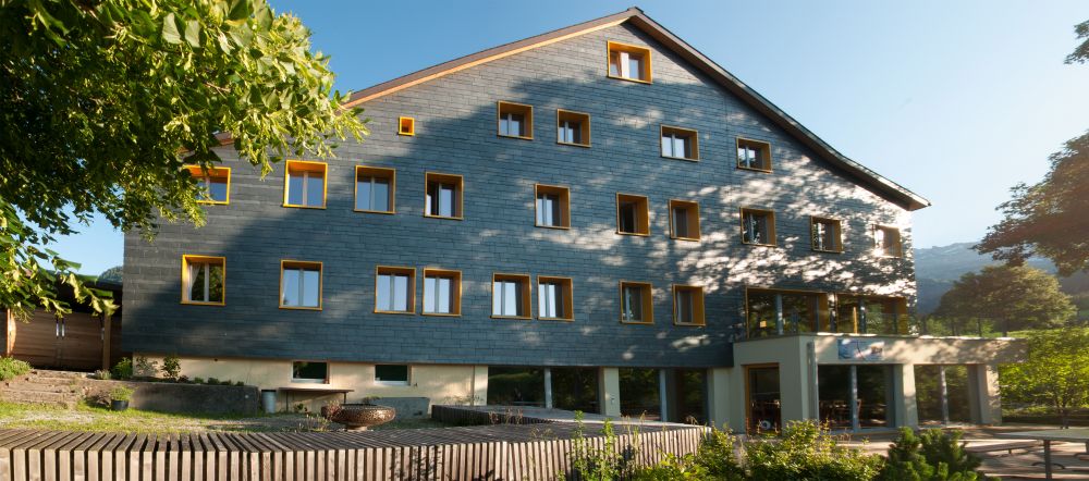 Das Karunahaus im Toggenburg mit schwarzen Schieferplatten und gelben Fensterläden